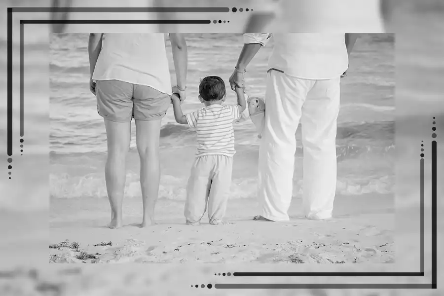 Eine Familie steht am Strand, Hand in Hand mit ihrem Kind. Das Bild ist schwarz-weiß